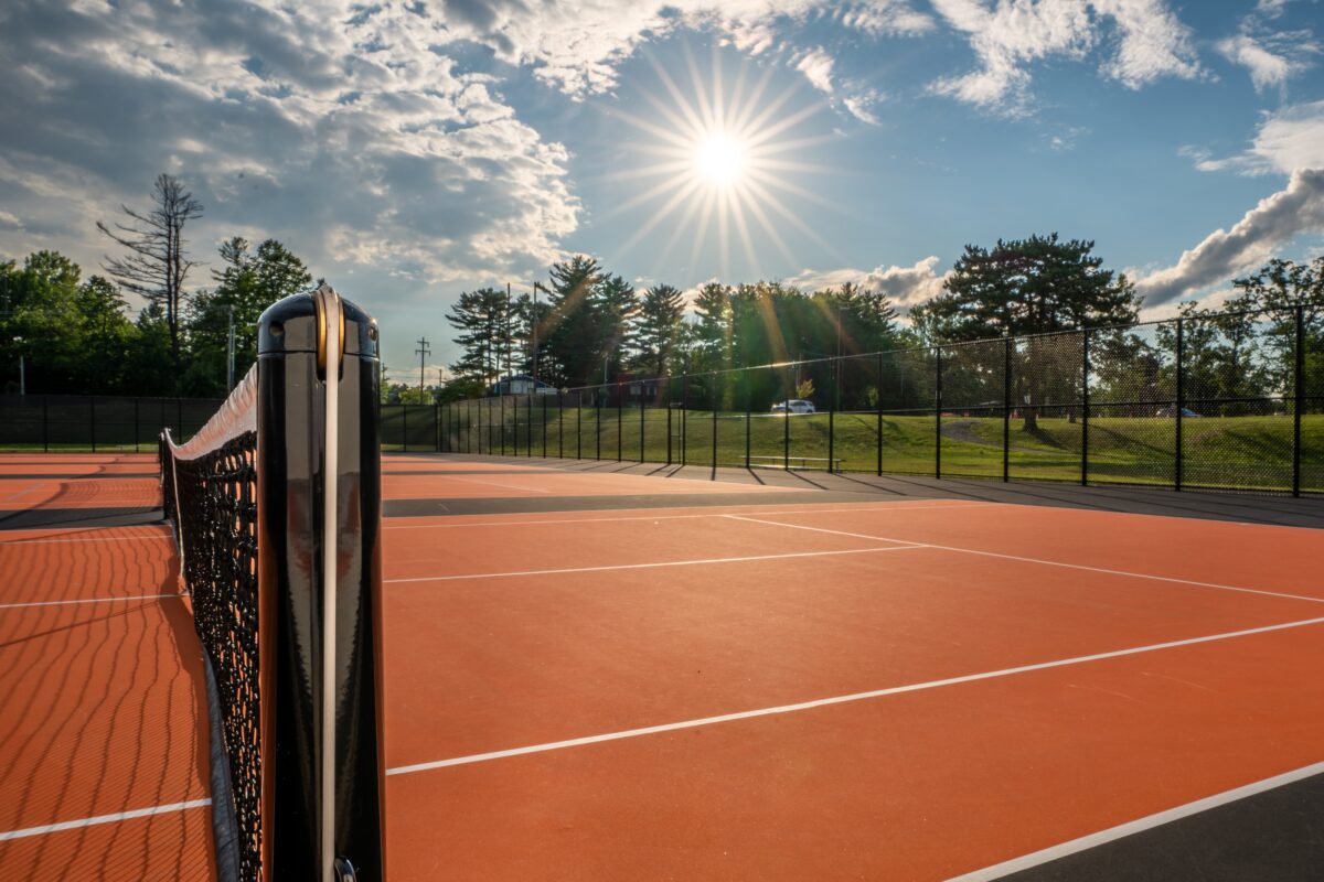 Tennis court and net, sun in the background, trees on horizon