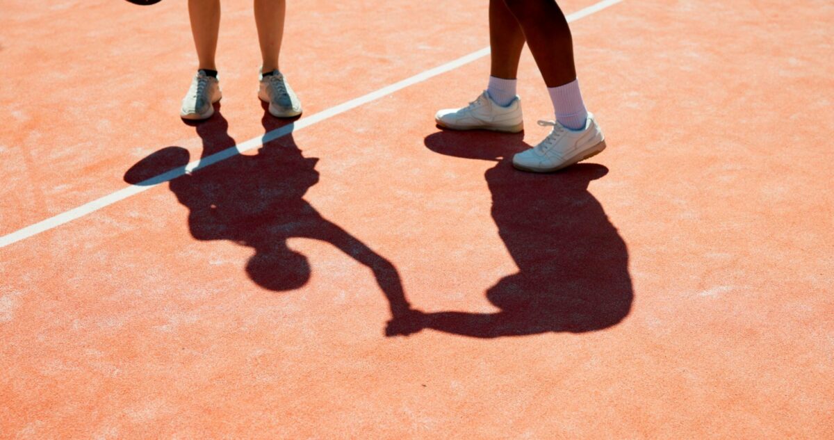 view of 2 people wearing tennis shoes standing on a tennis court.